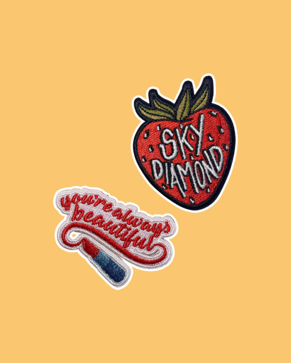 Two embroidered patches inspired by Sally Thorne's "The Hating Game". One patch says "you're always beautiful" with red lipstick. The other patch says "Sky Diamond" on a strawberry.
