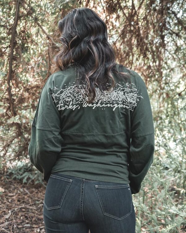 Close up of model wearing a dark green long sleeve shirt with a white design across shoulders.