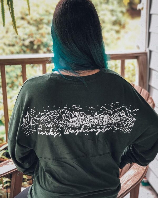 Forks, Washington Game Day Jersey - Game Day Close up of model wearing a dark green long sleeve shirt with a white design across shoulders.