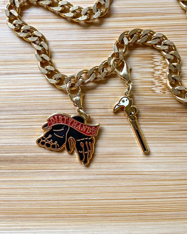 Two gold charms on a gold chain in the shape of gloves and a skull tipped cane.